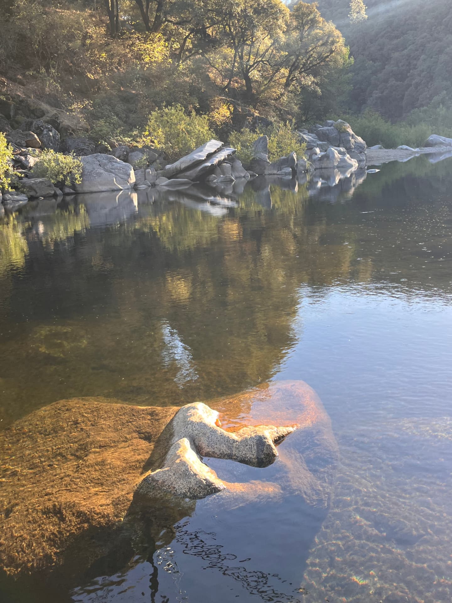 A quiet river reflecting sunlit trees and granite rocks